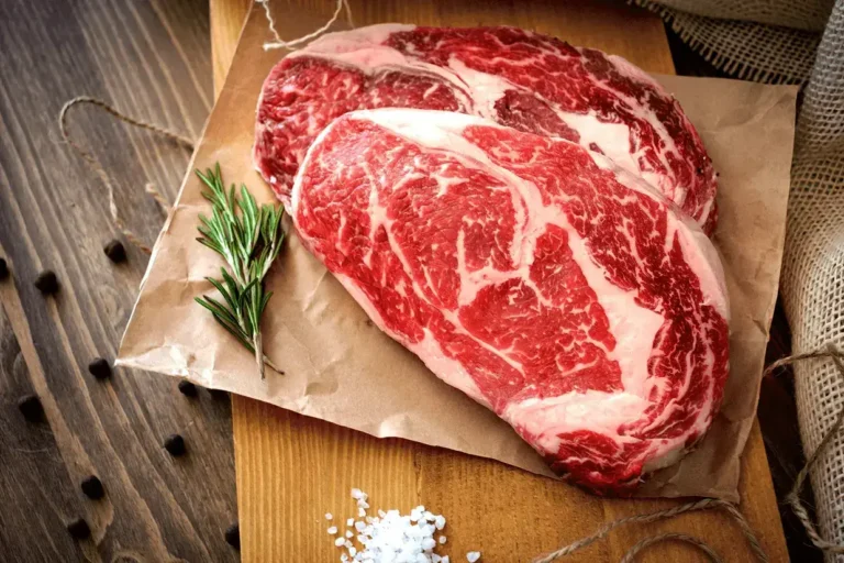 Two raw rib eye steak on a wooden Board on a table prepared for the grill. Top view rustic style
