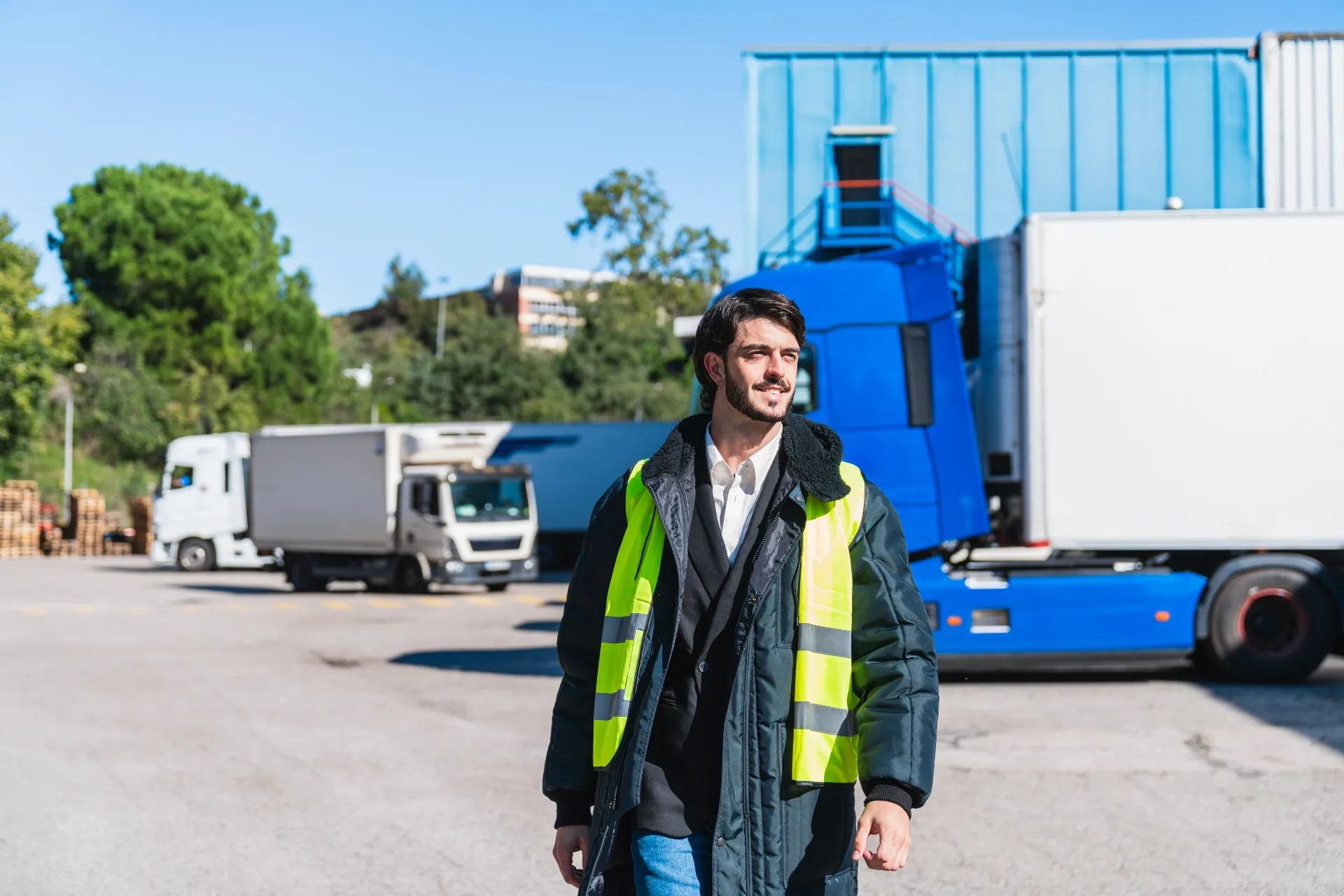 Truck driver with a beard wearing a fluorescent vest and winter jacket in a cold storage warehouse truck park