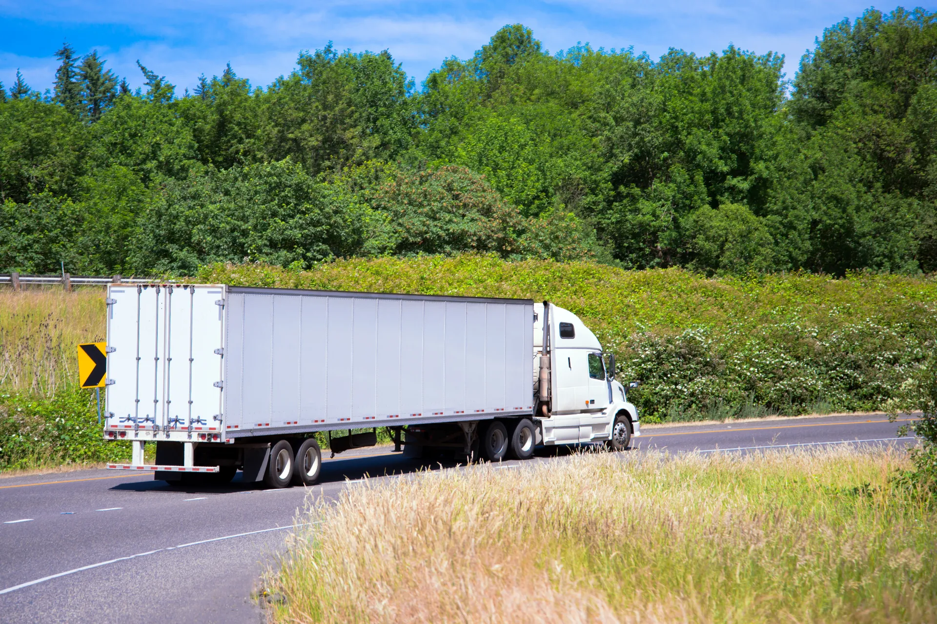 White semi truck modern trailer on turn road around green